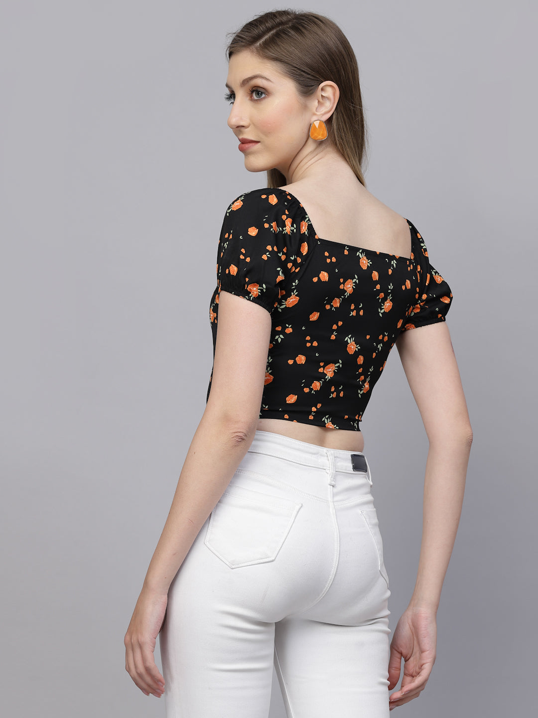 Woman wearing a black floral top and white pants on a gray background