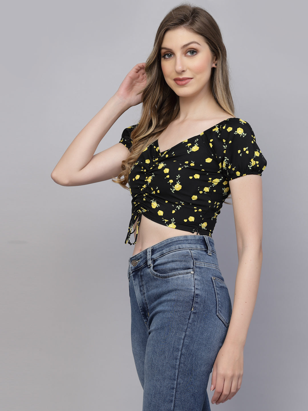 Woman wearing a black floral top and blue jeans on a gray background