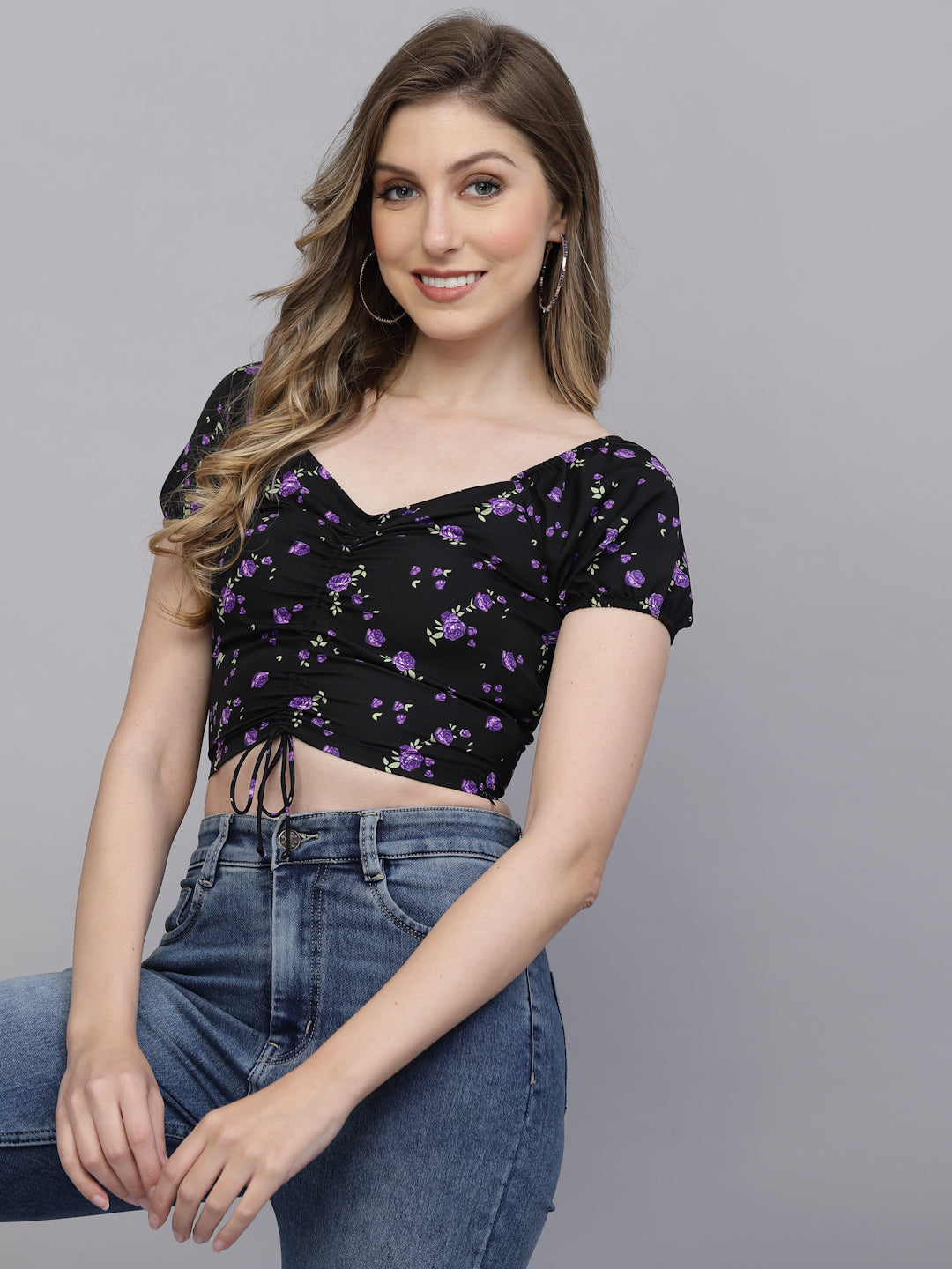 Woman wearing a black floral crop top and blue jeans on a gray background