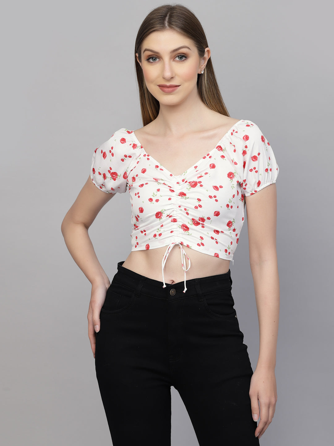 Woman wearing a white crop top with red floral patterns and black pants on a gray background