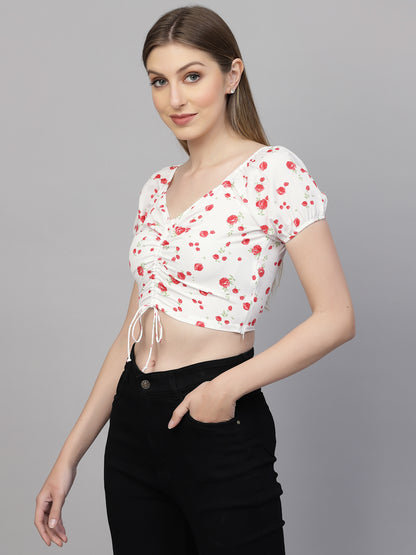 Woman wearing a white floral top with red flowers and black pants on a gray background