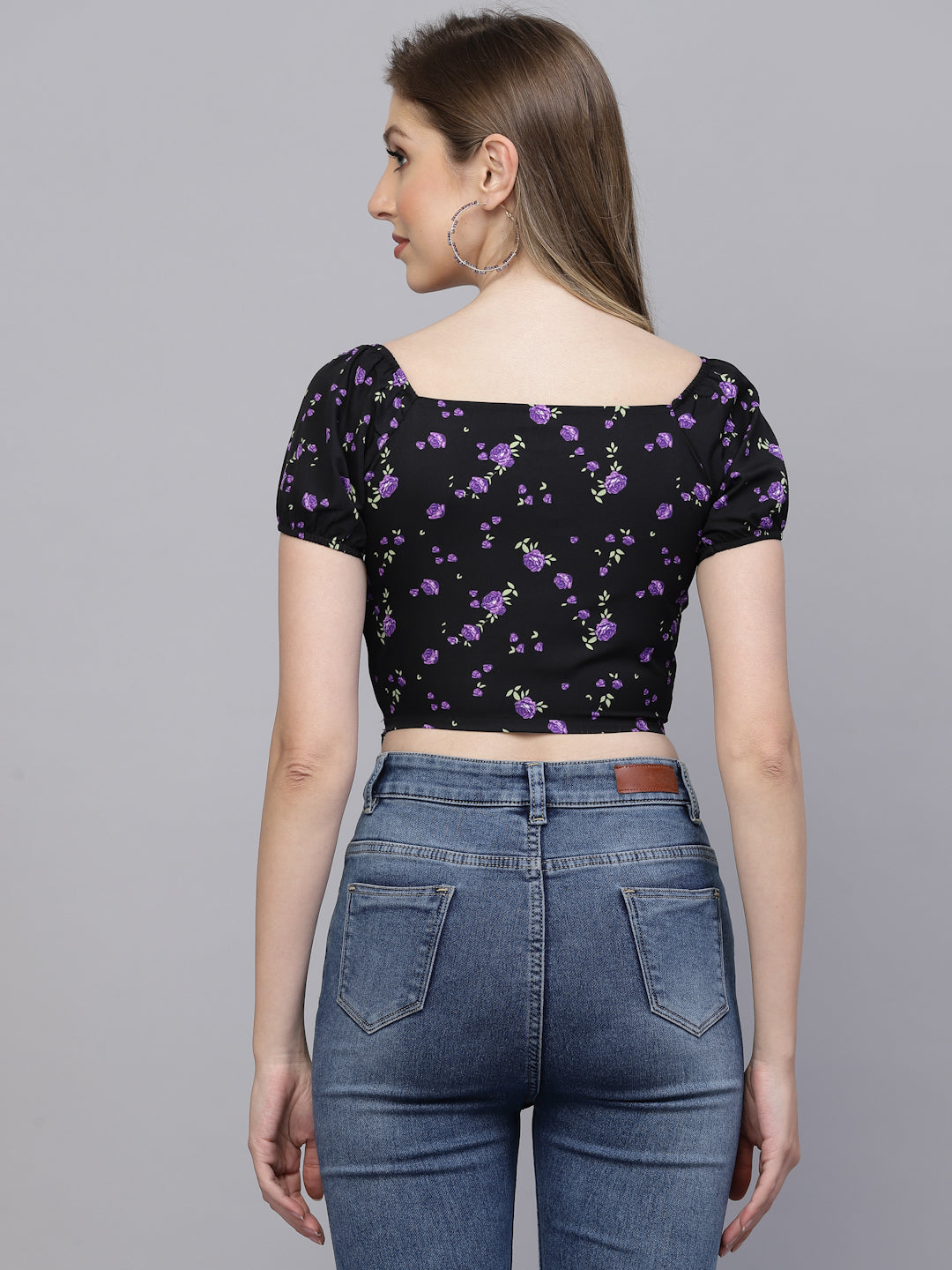 Woman wearing a black floral top and blue jeans on a gray background