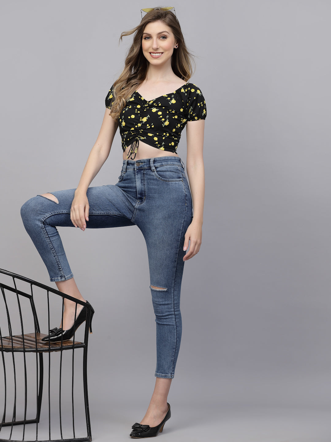 Woman wearing a black floral top and blue jeans on a gray background