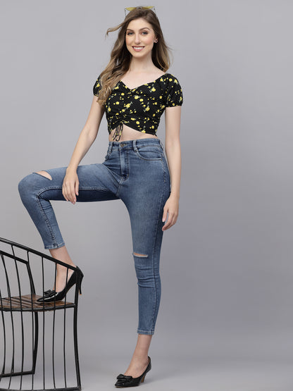 Woman wearing a black floral top and blue jeans on a gray background