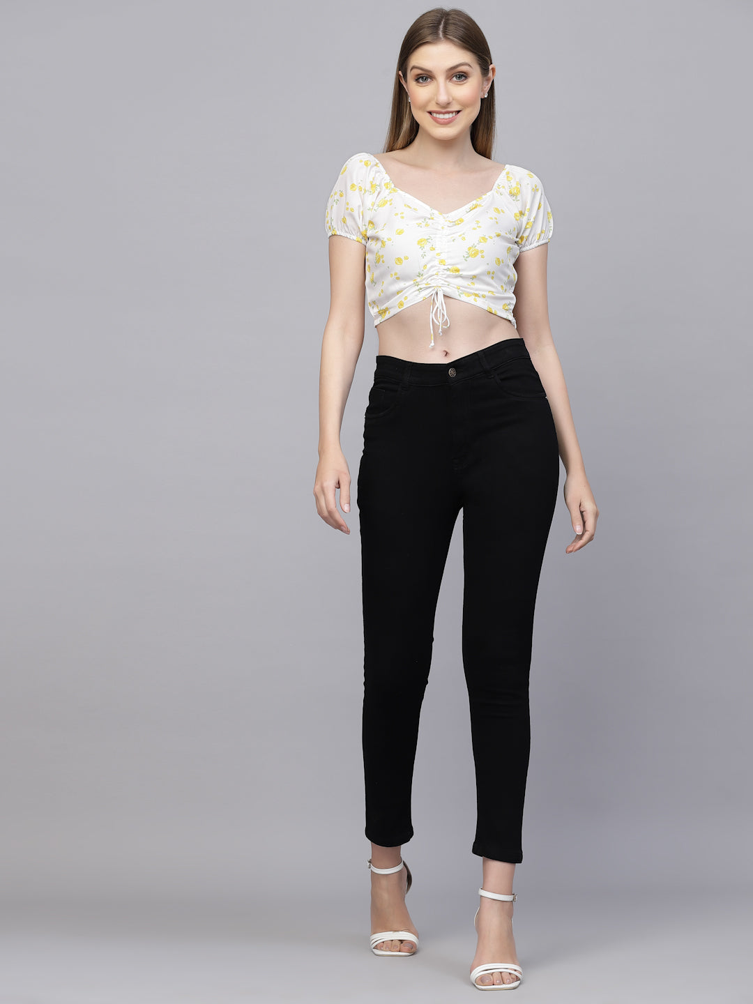 Woman wearing a white floral top and black pants on a gray background