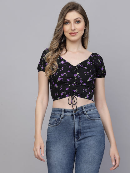 Woman wearing a black floral crop top and blue jeans on a gray background