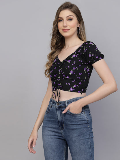 Woman wearing a black floral crop top and blue jeans on a gray background