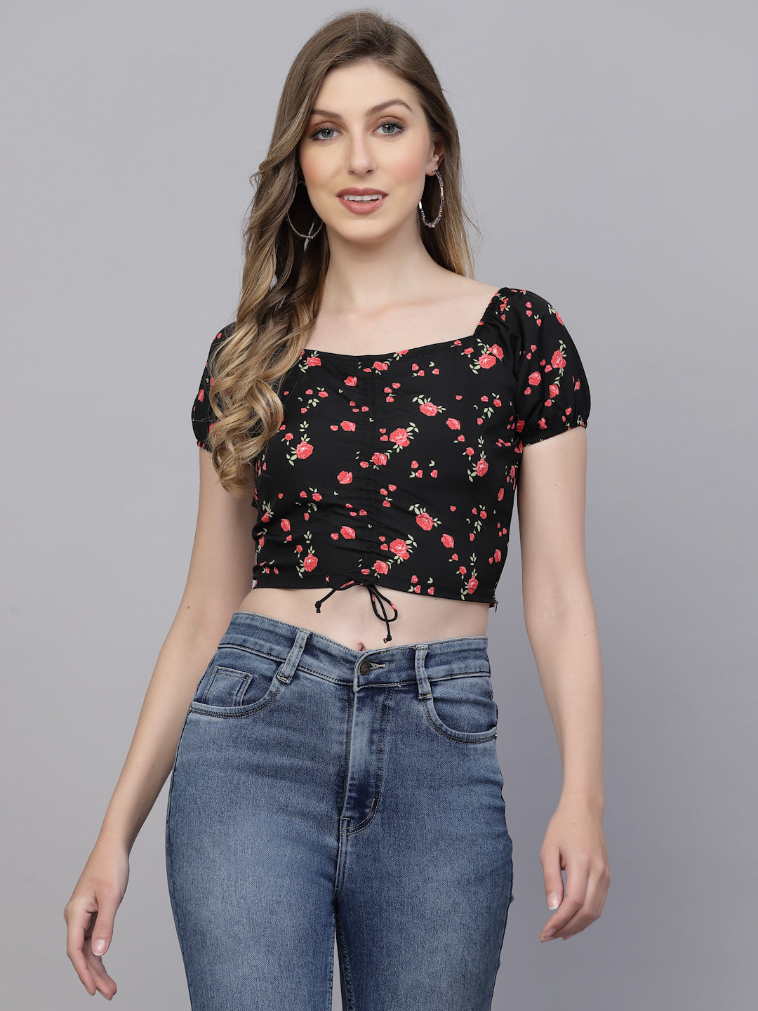 Woman wearing a black & pink floral crop top and blue jeans on a gray background