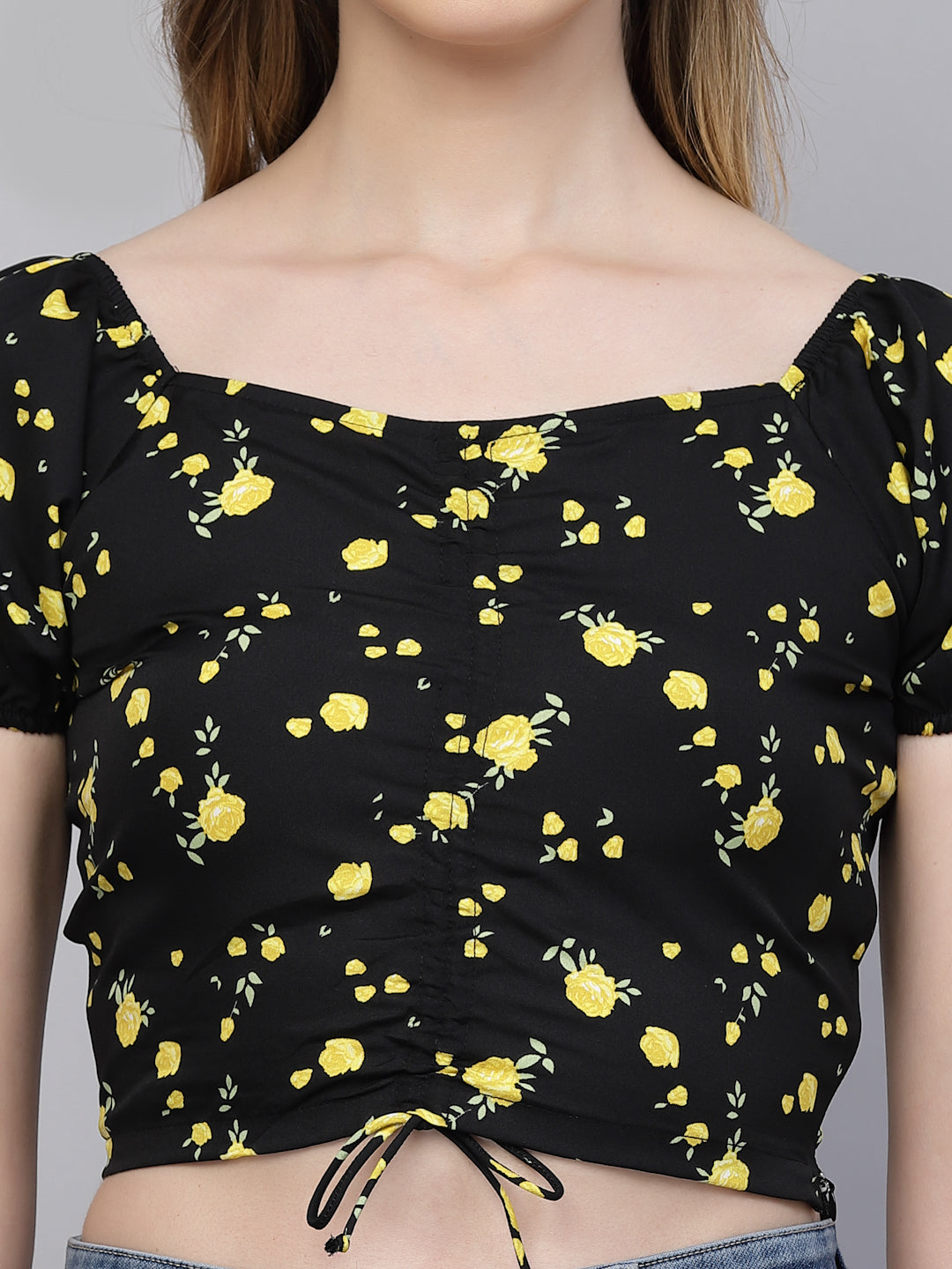 Black top with yellow floral pattern worn by a person on a gray background
