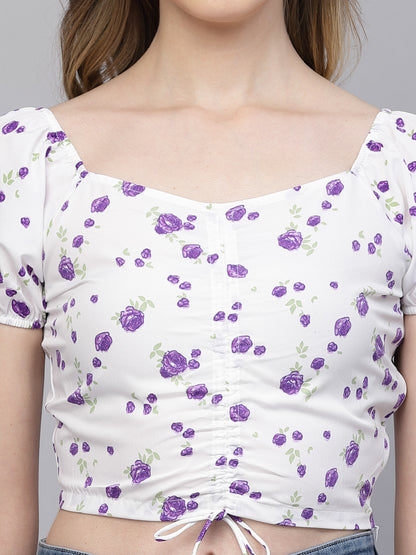 White crop top with purple floral pattern worn by a person on a plain background