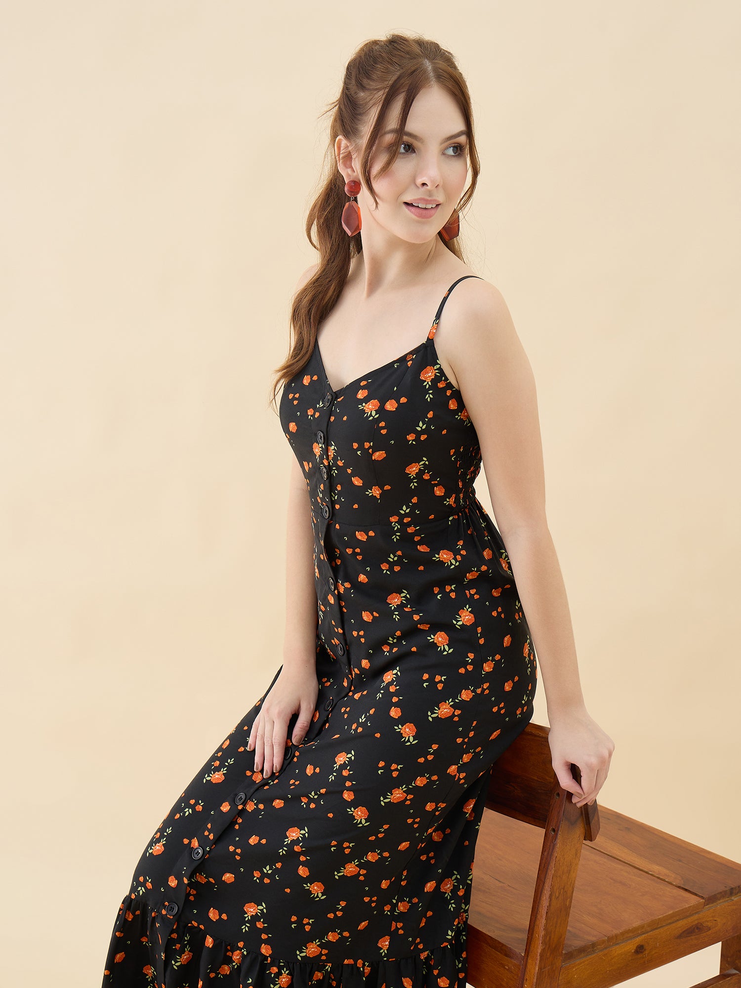Woman wearing a black floral dress sitting on a wooden chair against a beige background