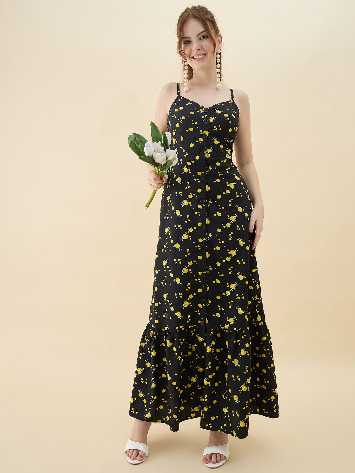 Woman wearing a black dress with yellow floral pattern holding flowers against a beige background