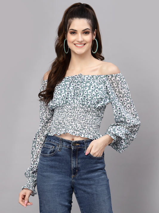 Woman wearing a green floral off-shoulder top and jeans on a gray background