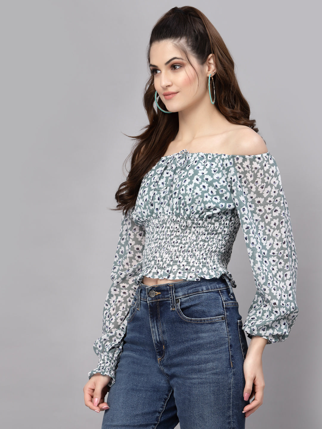 Woman wearing a green floral off-shoulder top and jeans on a gray background