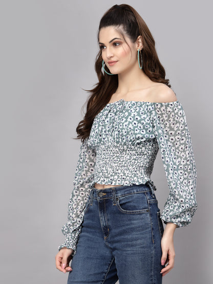 Woman wearing a green floral off-shoulder top and jeans on a gray background