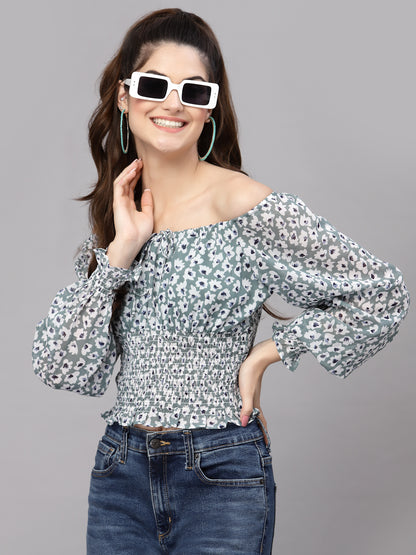 Woman wearing a green floral off-shoulder top and jeans with sunglasses on a gray background