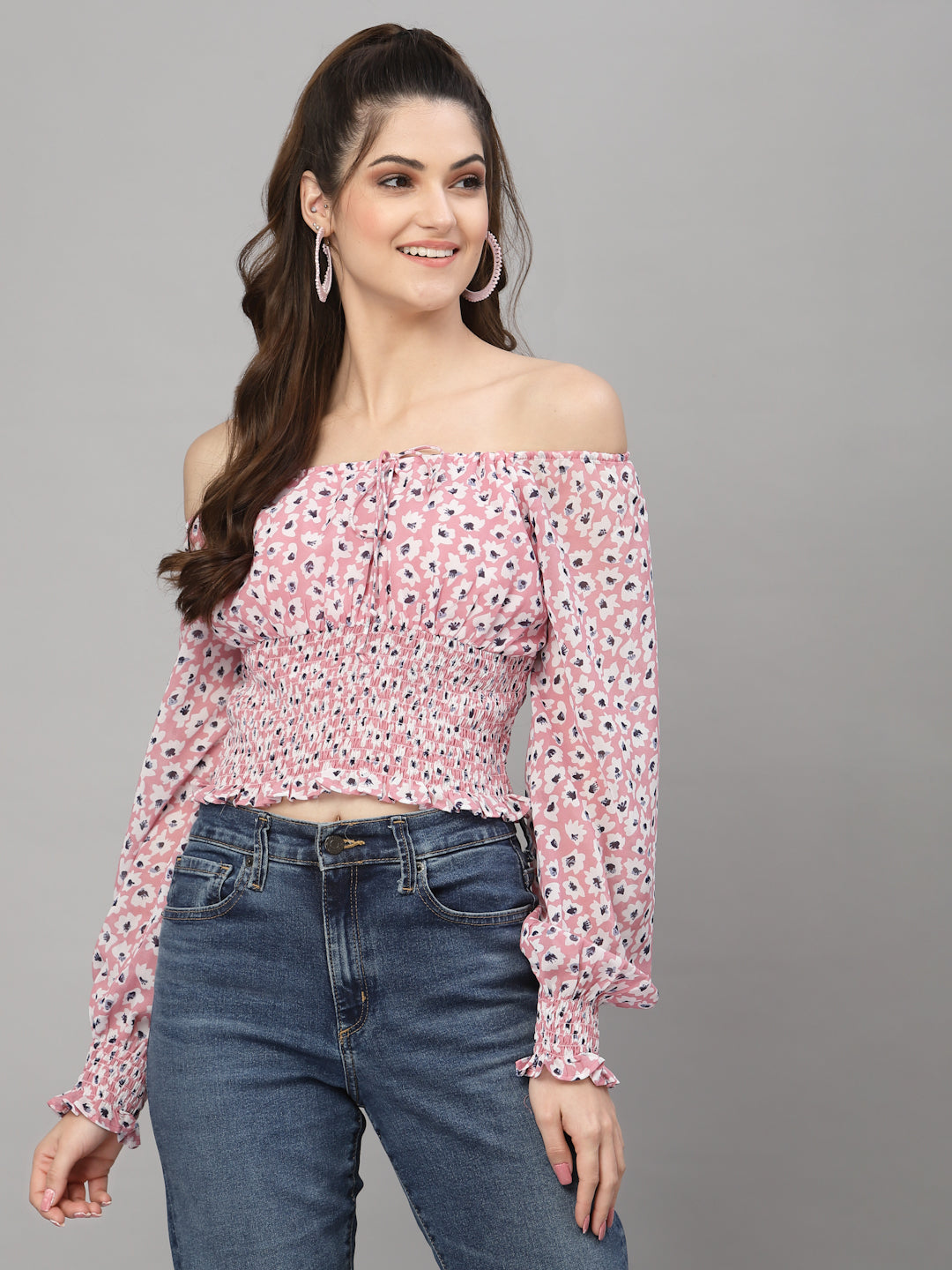 Woman wearing a pink floral off-shoulder top and blue jeans on a gray background