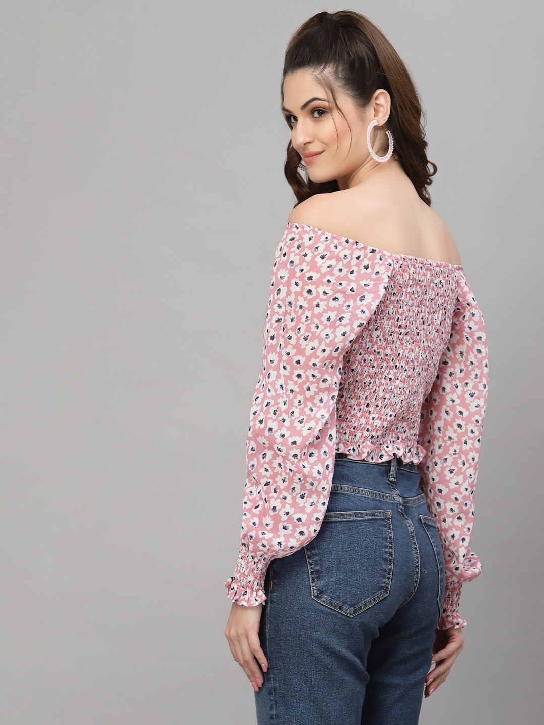Woman wearing a pink floral off-shoulder blouse and blue jeans on a gray background