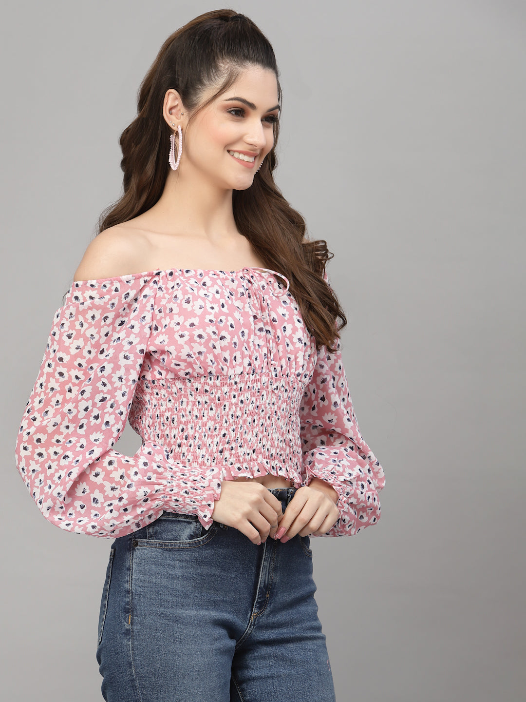 Woman wearing a pink floral off-shoulder top and blue jeans on a gray background
