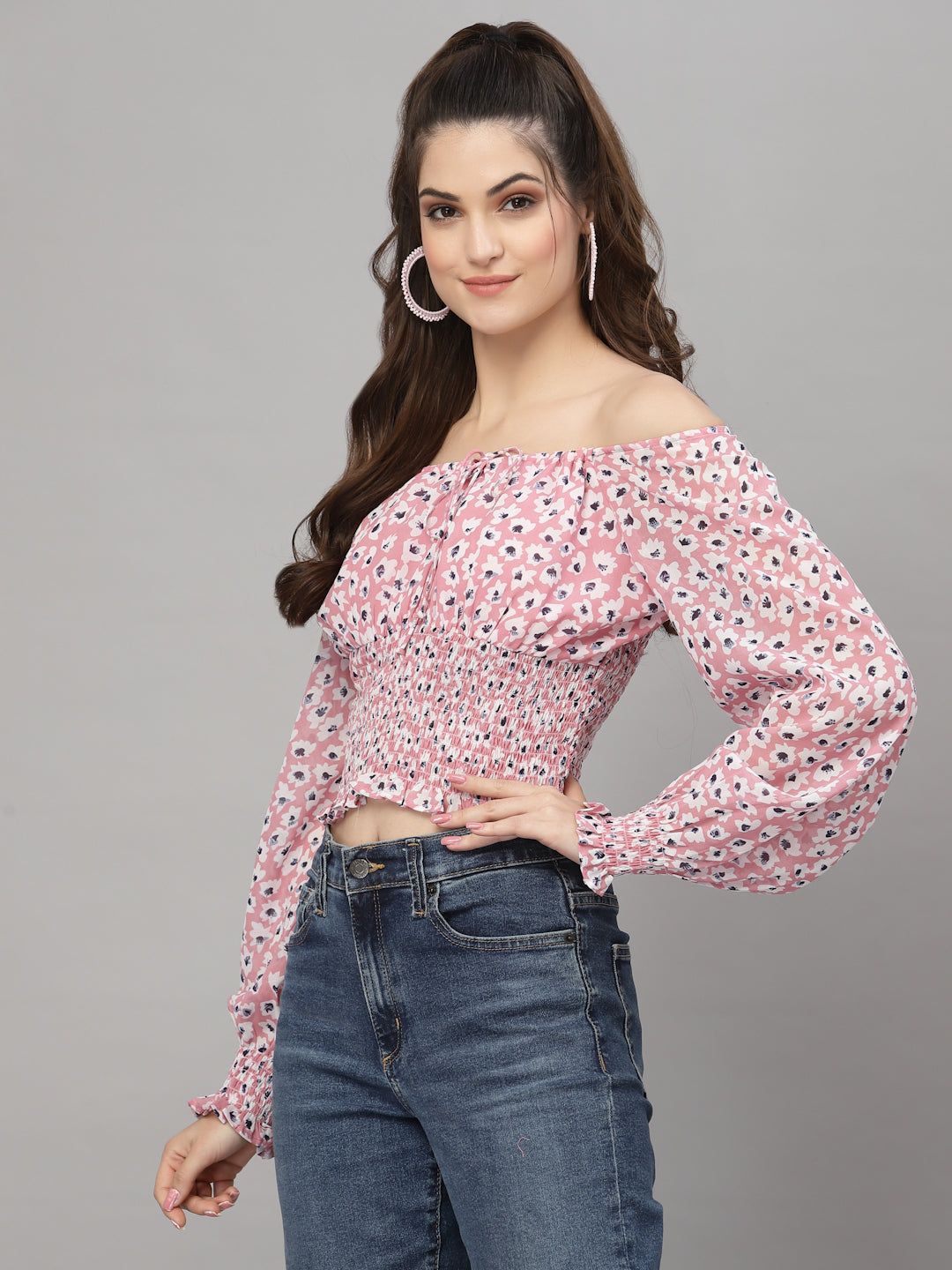 Woman wearing a pink floral off-shoulder top and blue jeans on a gray background