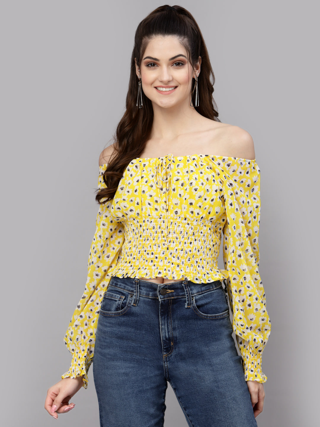 Woman wearing a yellow floral off-shoulder top and blue jeans on a gray background
