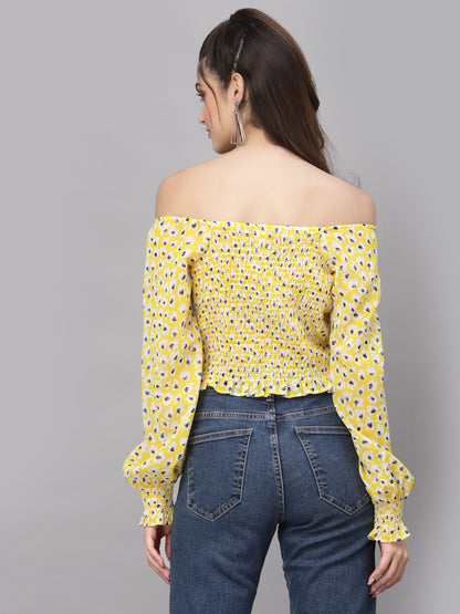 Woman wearing a yellow off-shoulder top with a floral pattern and blue jeans on a gray background
