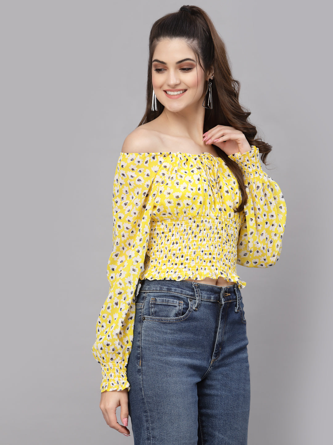 Woman wearing a yellow floral off-shoulder top and blue jeans on a gray background