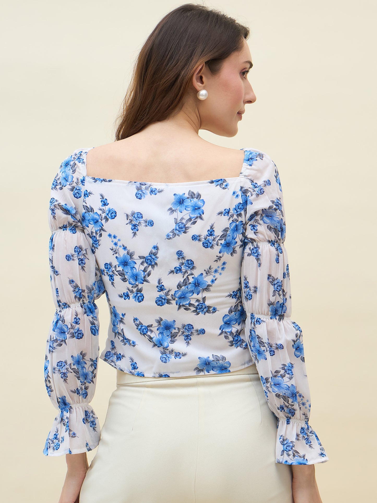 Woman wearing a floral top with blue flowers on a plain background