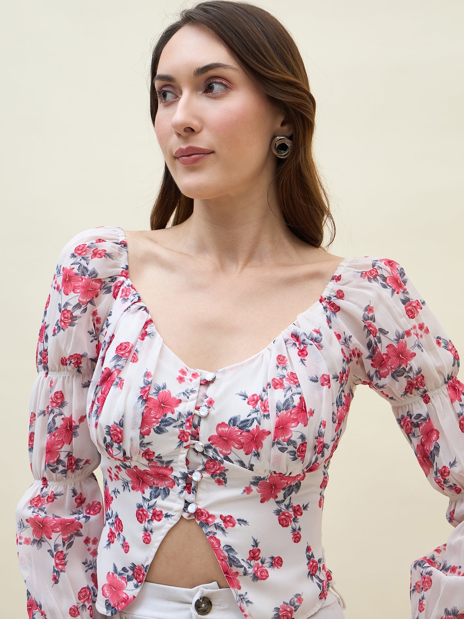 Woman wearing a white & pink floral top with puff sleeves against a plain background
