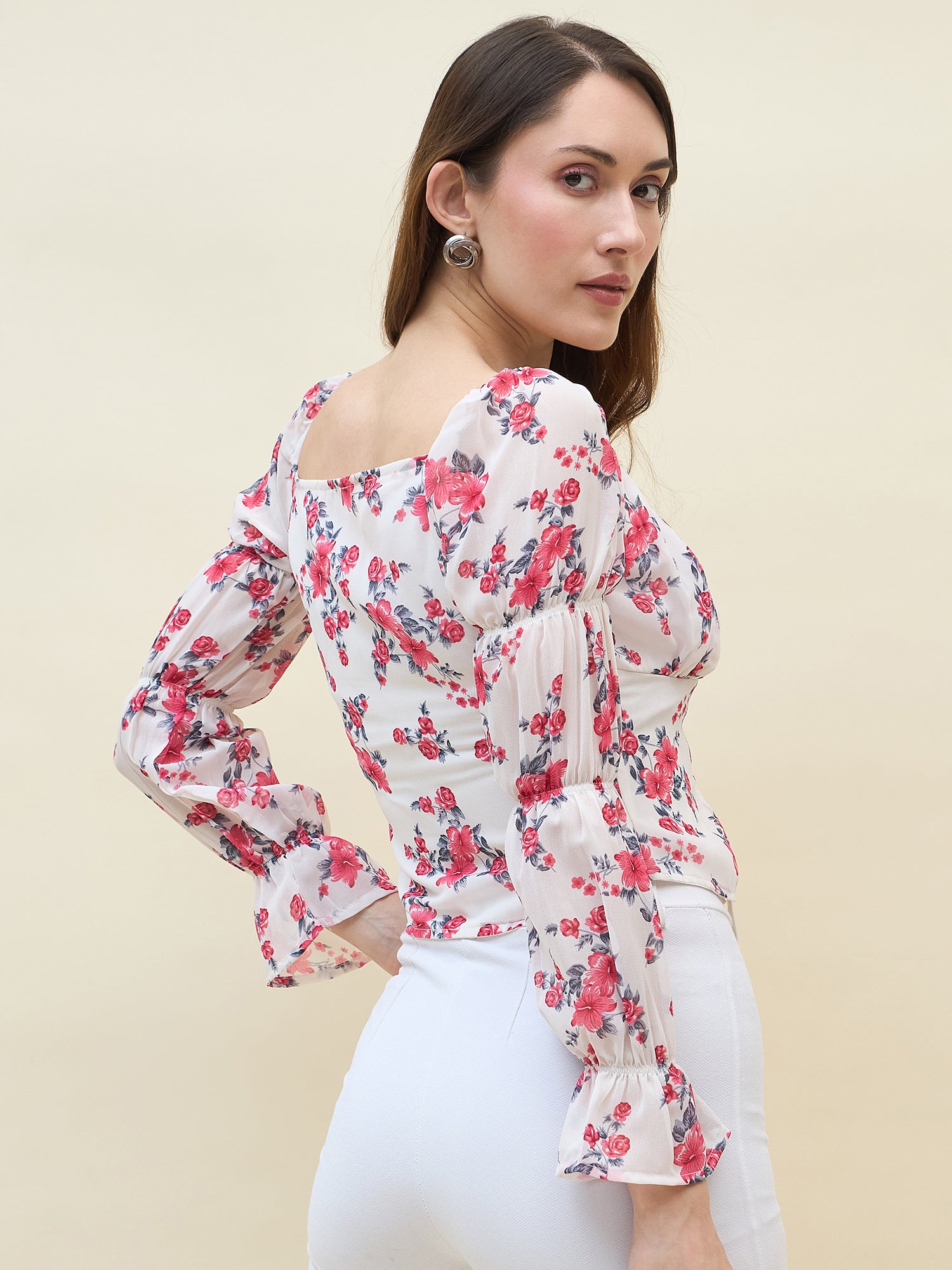 Woman wearing a white & pink floral top with long sleeves on a beige background
