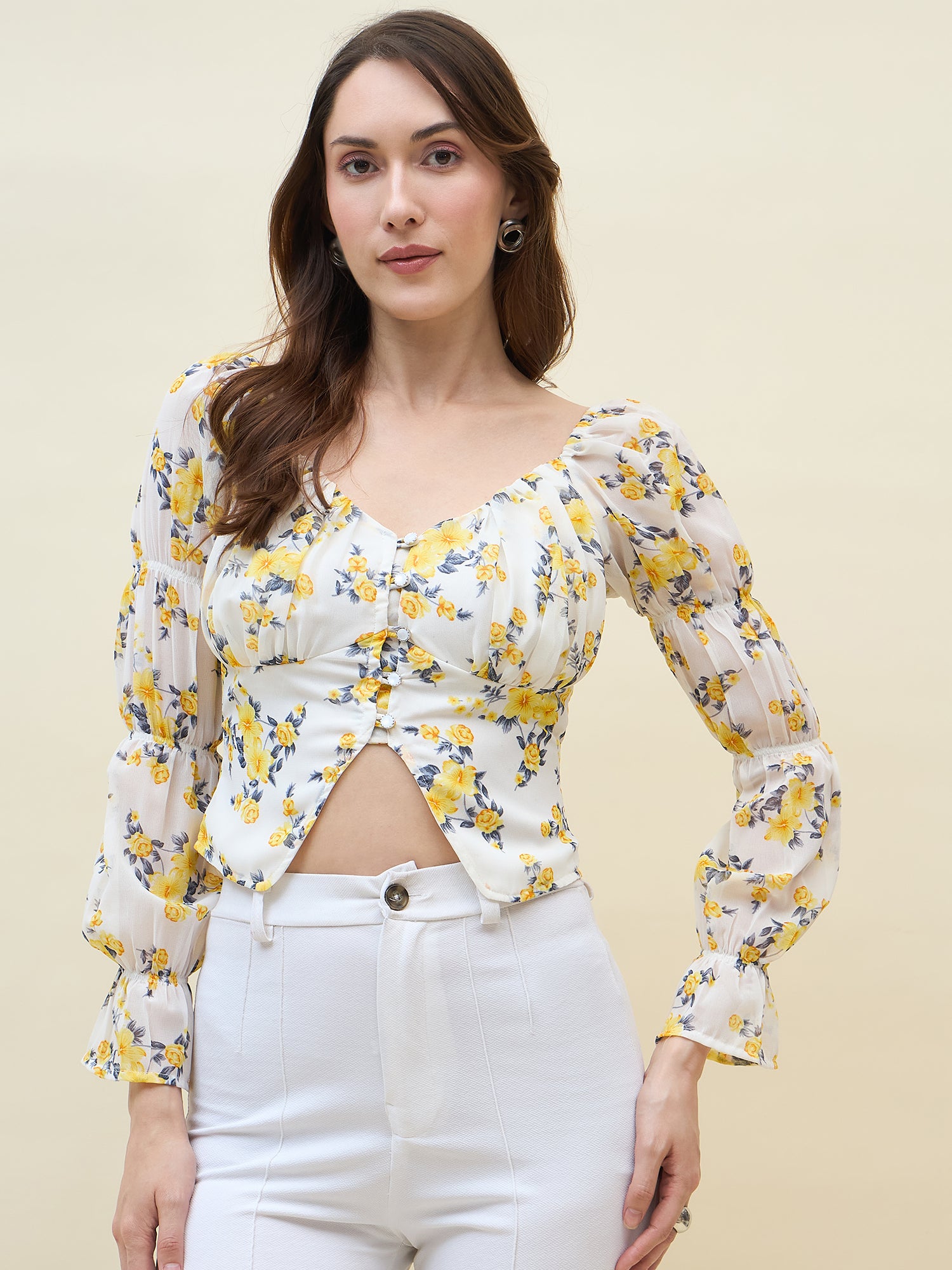 Woman wearing a white & yellow floral long-sleeve top and white pants against a beige background