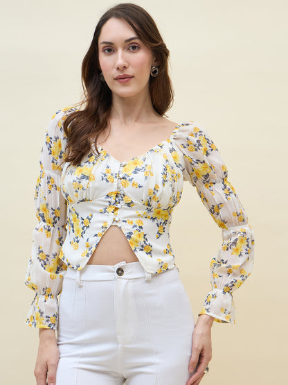 Woman wearing a white & yellow floral long-sleeve top and white pants against a beige background
