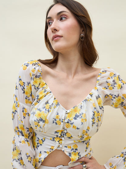 Woman wearing a white & yellow floral long-sleeve top against a plain background