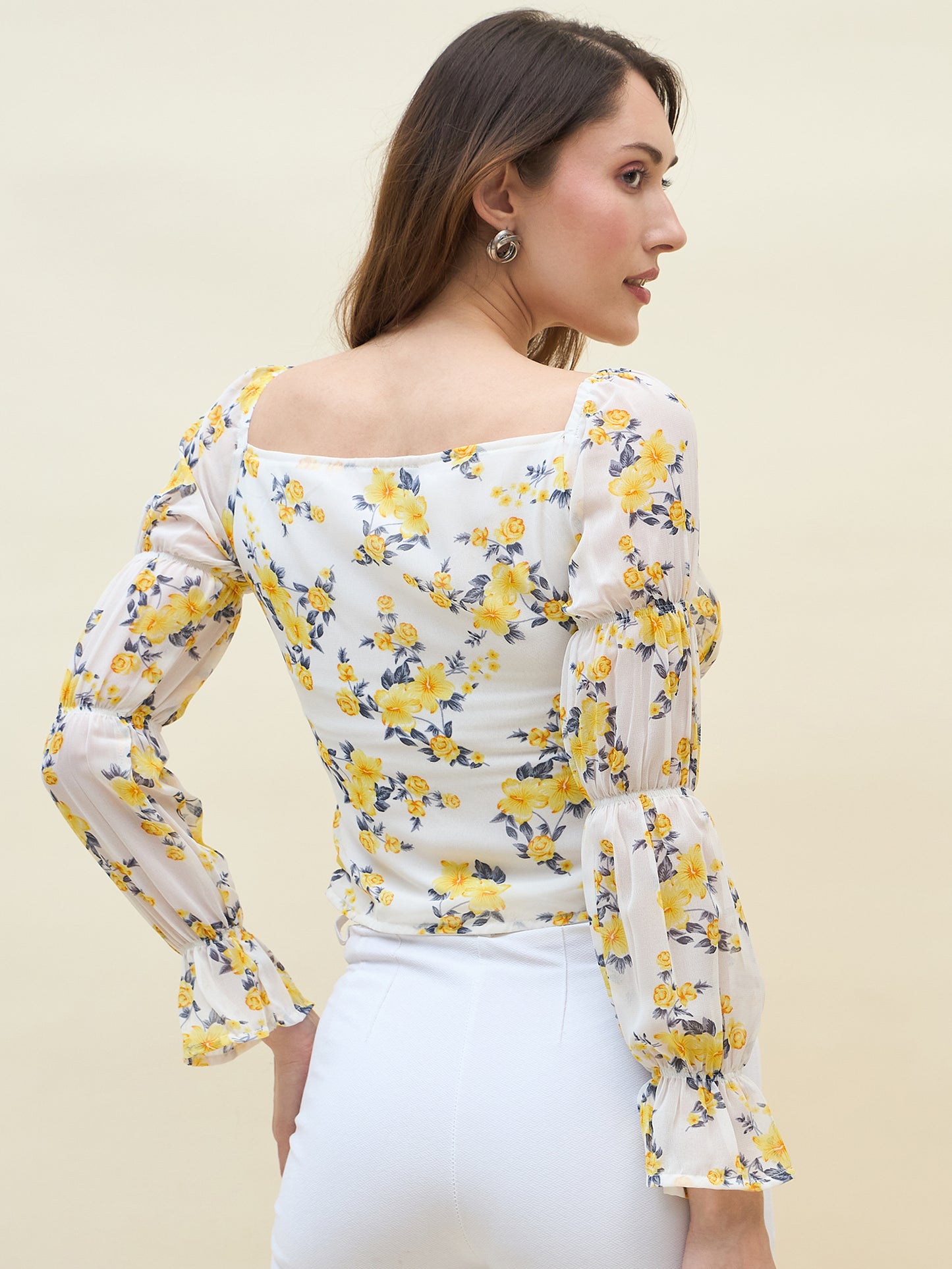 Woman wearing a white floral top with yellow flowers on a beige background