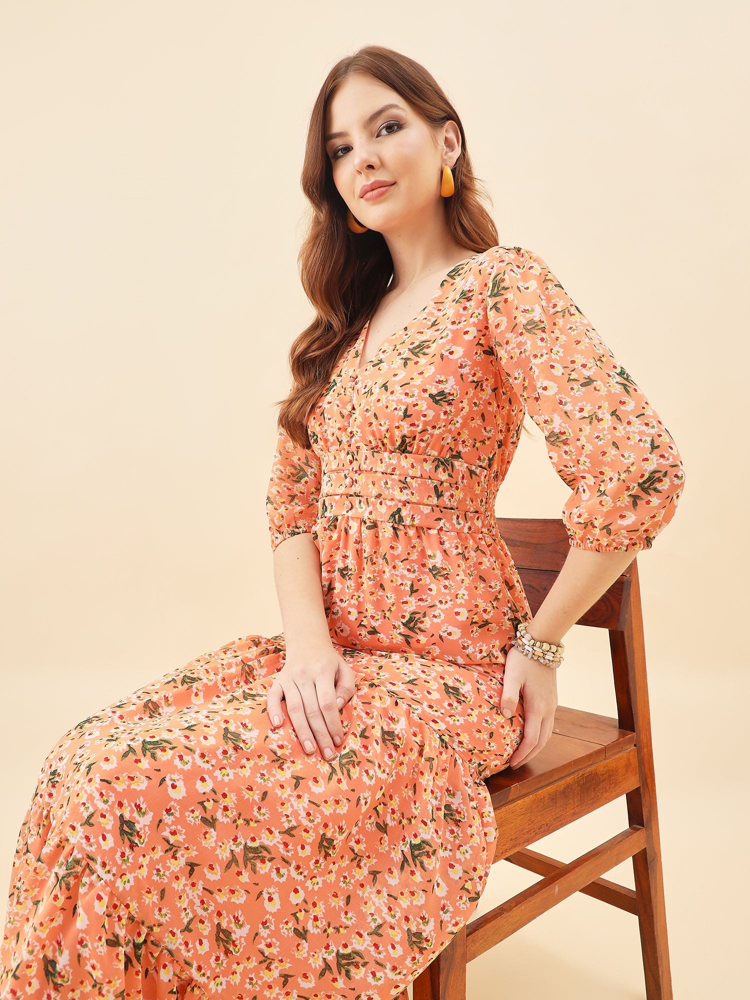 Woman in a orange floral dress sitting on a wooden chair against a beige background