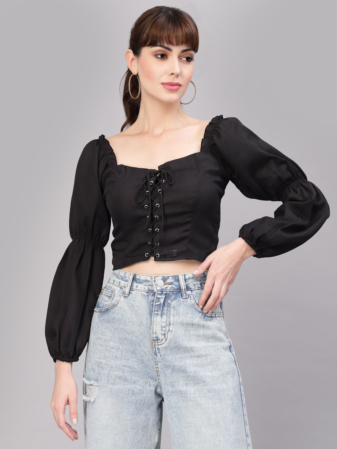 Woman wearing a black top with puffed sleeves and high-waisted jeans on a gray background
