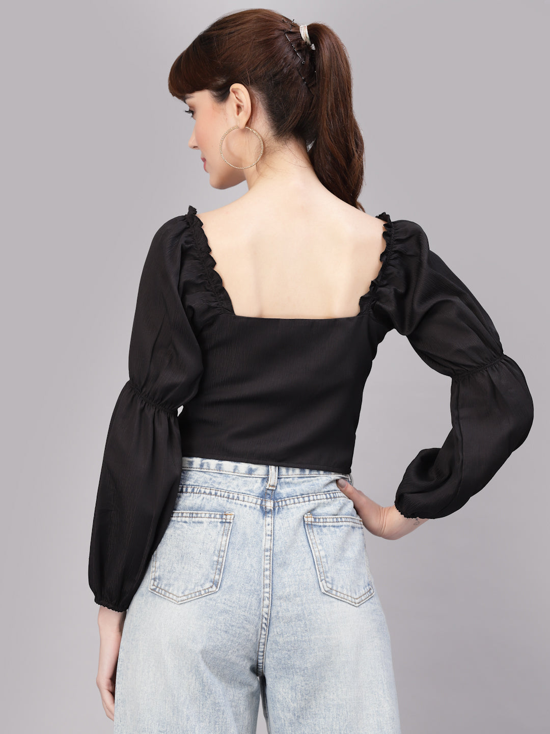 Woman wearing a black top with puffed sleeves and light blue jeans on a gray background