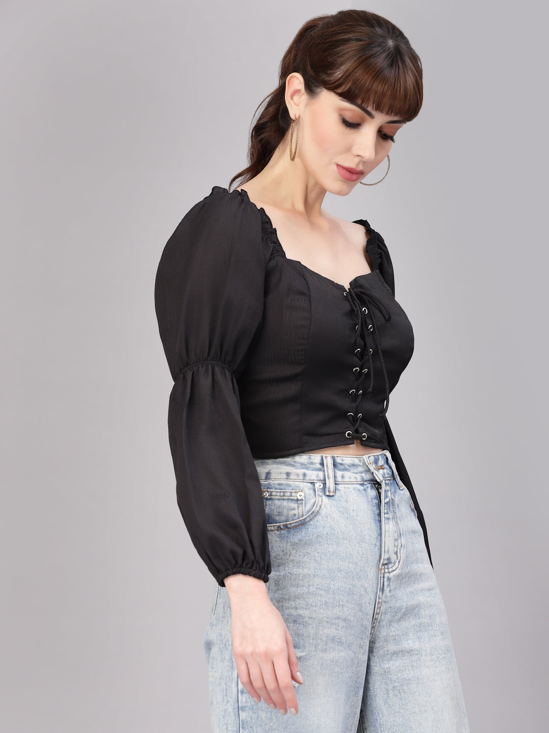 Woman wearing a black top with long sleeves and a high neckline, standing against a gray background.