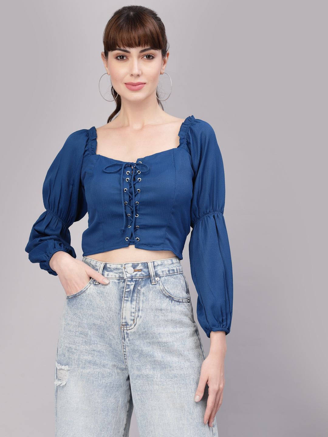 Woman wearing a blue top with puffed sleeves and high-waisted jeans on a gray background