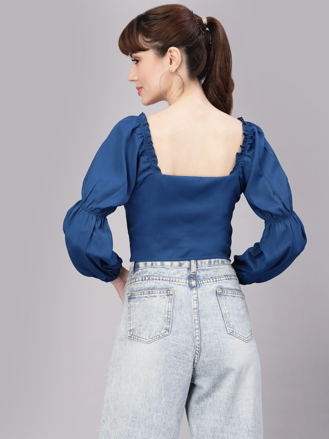 Woman wearing a blue top with puffed sleeves and light blue jeans on a gray background