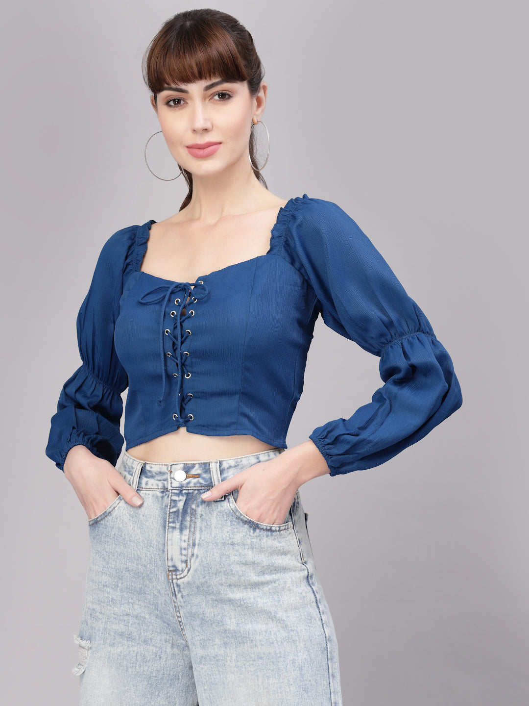 Woman wearing a blue top with long sleeves and high-waisted jeans on a gray background