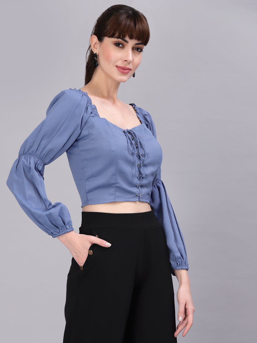 Woman wearing a light blue top with puffed sleeves and black pants on a gray background