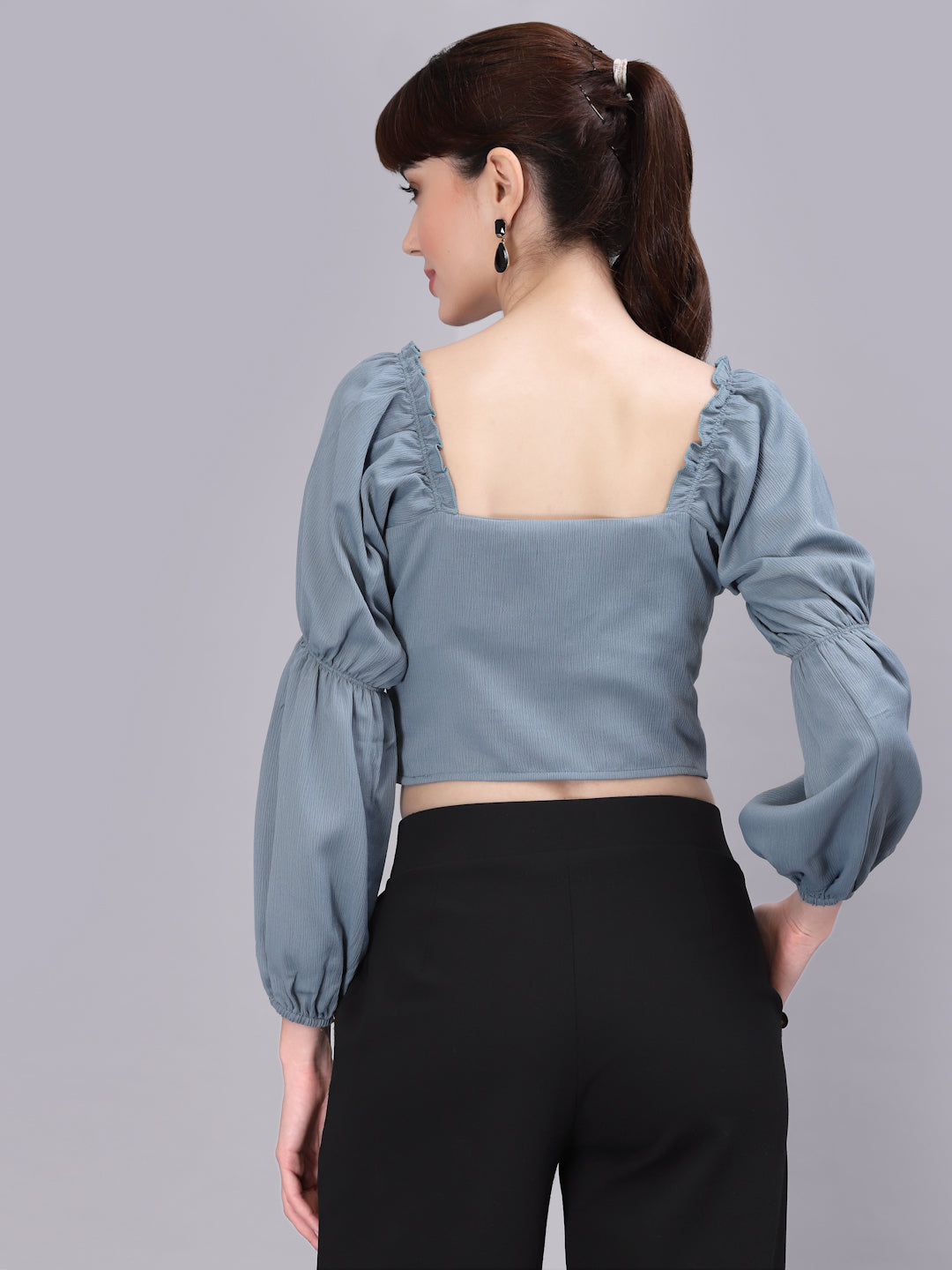 Woman wearing a light green top with puffed sleeves and black pants on a gray background