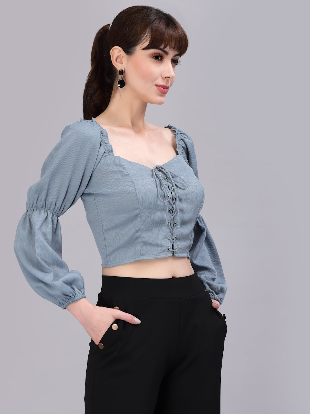 Woman wearing a light green top with puffed sleeves and black pants on a gray background