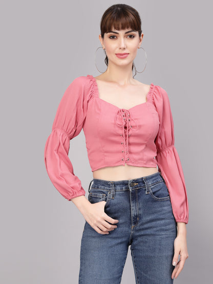 Woman wearing a peach blouse with long sleeves and blue jeans on a gray background