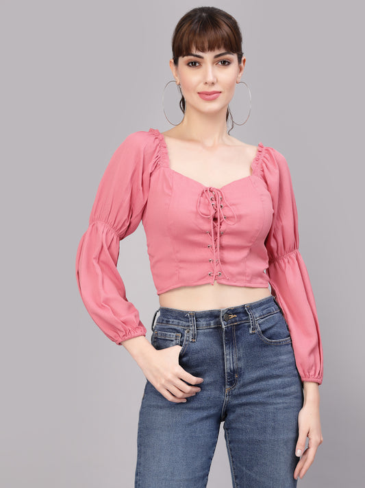 Woman wearing a peach blouse with long sleeves and blue jeans on a gray background