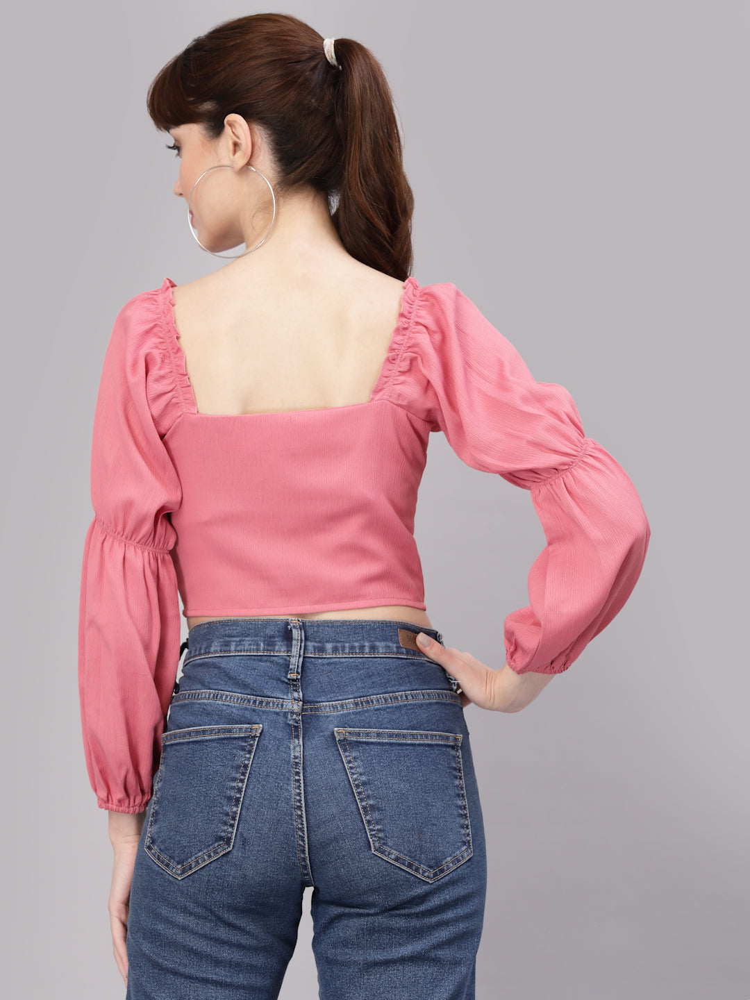 Person wearing a peach top with long sleeves and blue jeans on a gray background