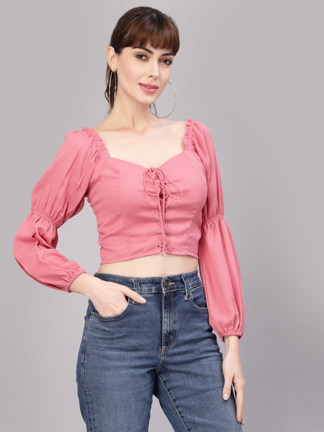 Woman wearing a peach top with long sleeves and blue jeans on a gray background