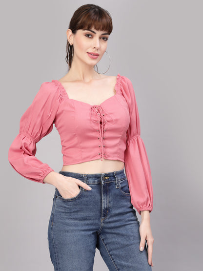 Woman wearing a peach top with long sleeves and blue jeans on a gray background