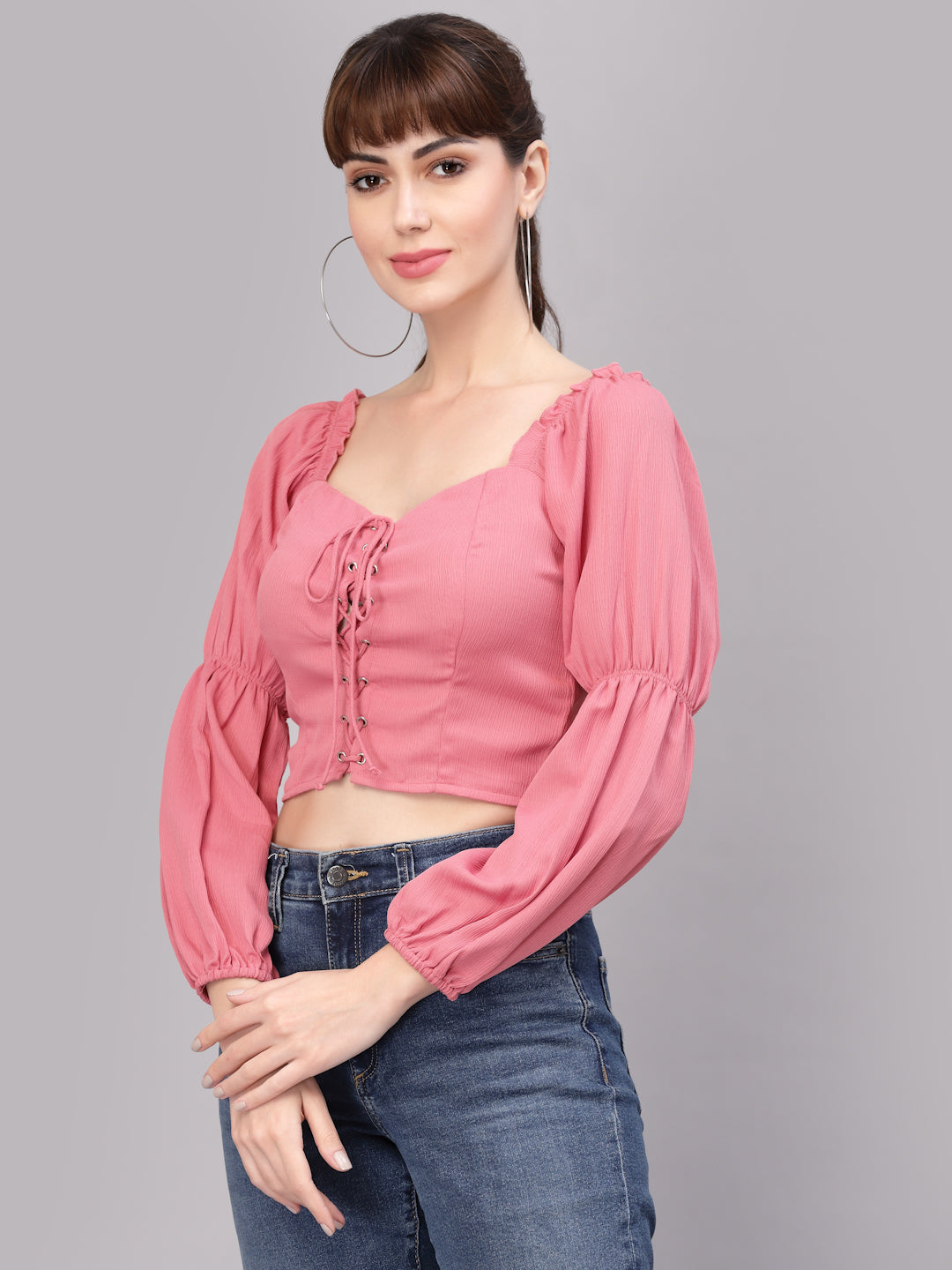 Woman wearing a peach top with long sleeves and blue jeans on a gray background